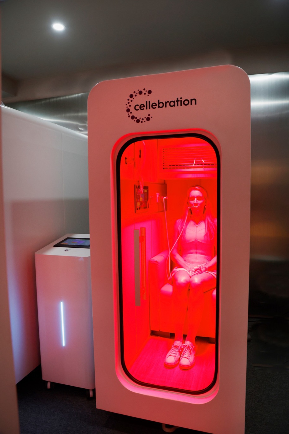 Inside a Cellebration hyperbaric chamber: a guest seated by the glass door under red light